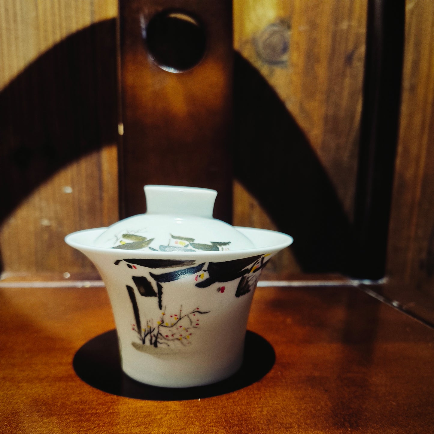 Close up view of handcrafted porcelain gaiwan with Wu Guanzhong inspired abstract painting, placed on a traditional Chinese oriental furniture
