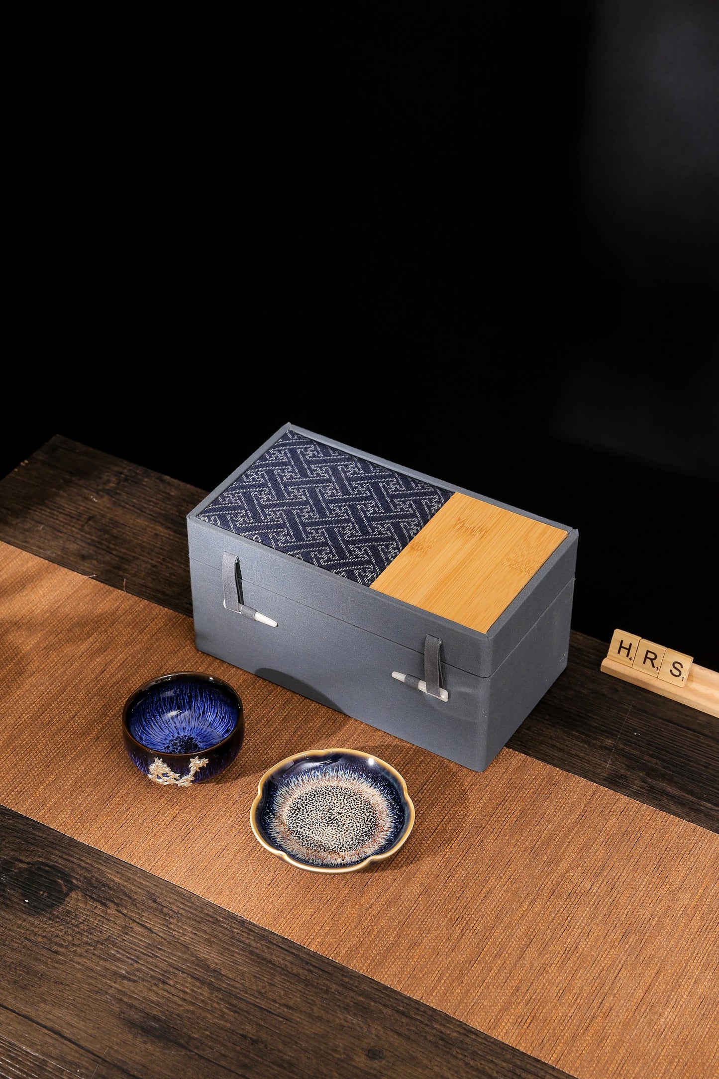 Handcrafted Jian Zhan tea cup with floral silver embellishment placed next to a matching decorative ceramic plate – luxury tea gift set"