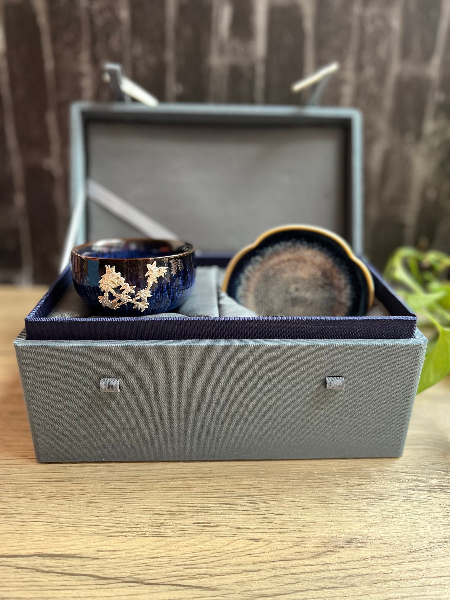 Blue ceramic cup and dish presented inside a gray gift box with button locks