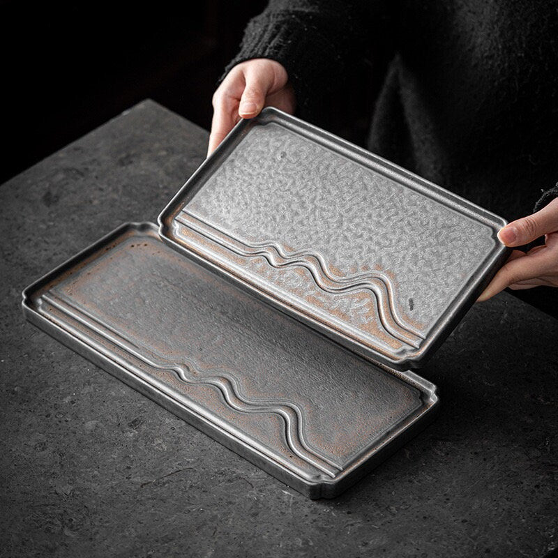 Hands holding a small size rectangular ceramic tea tray with water flow and mountain design_comes with gold glaze as the decor_picture showing 2 available sizes large and small