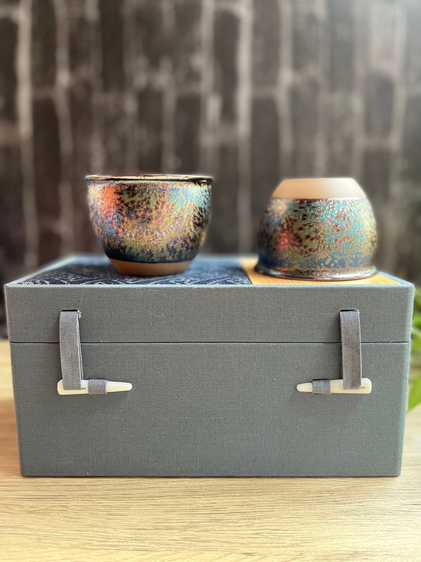 Pair of rainbow glazed ceramic cups presented inside decorative gray gift box.