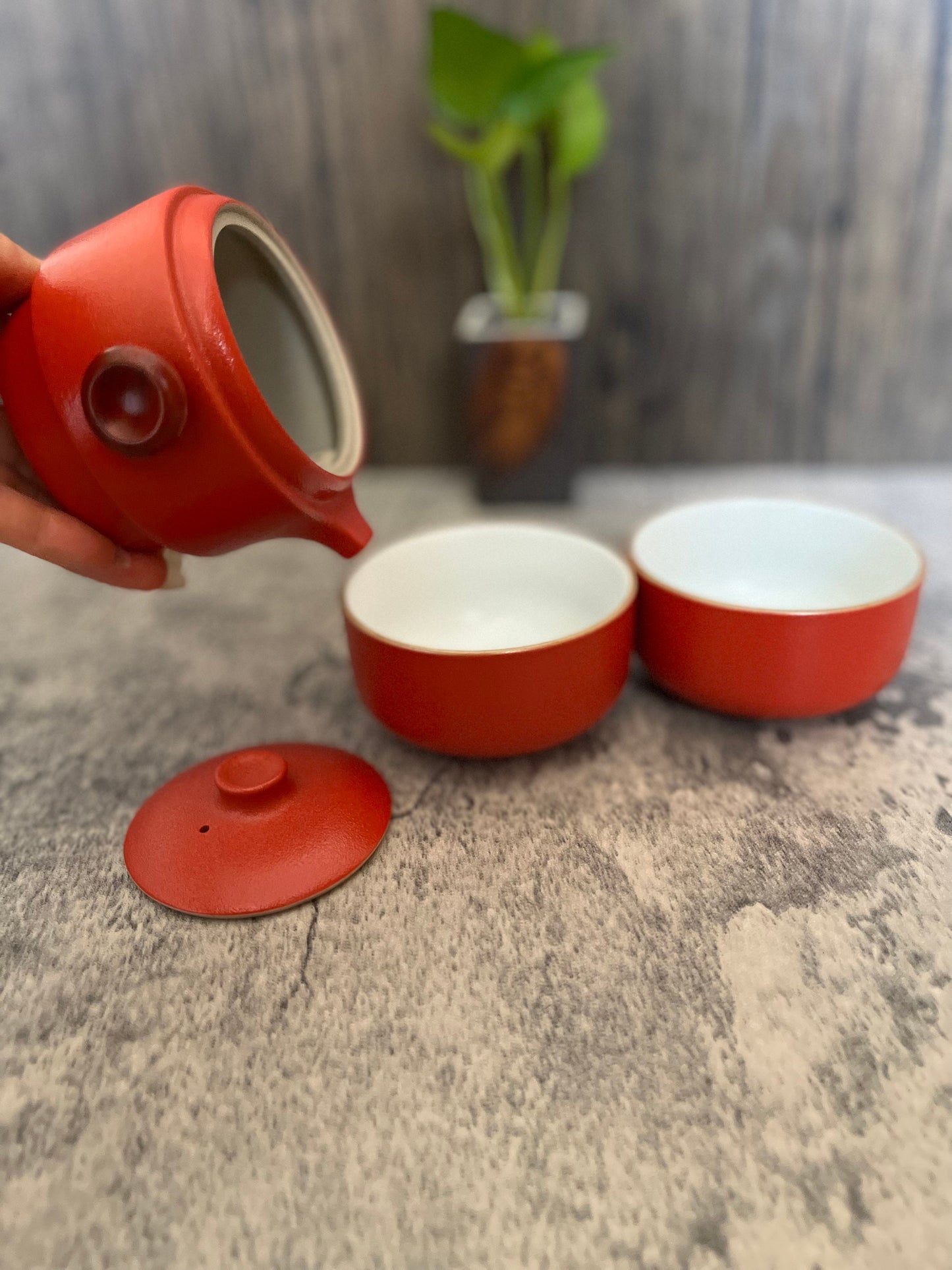 Portable ceramic teapot and tea cup travel set with red button design_all in one cup and kettle set_person showing how to use by pouring water from the teapot into cups_set from Home Relax Studio brand
