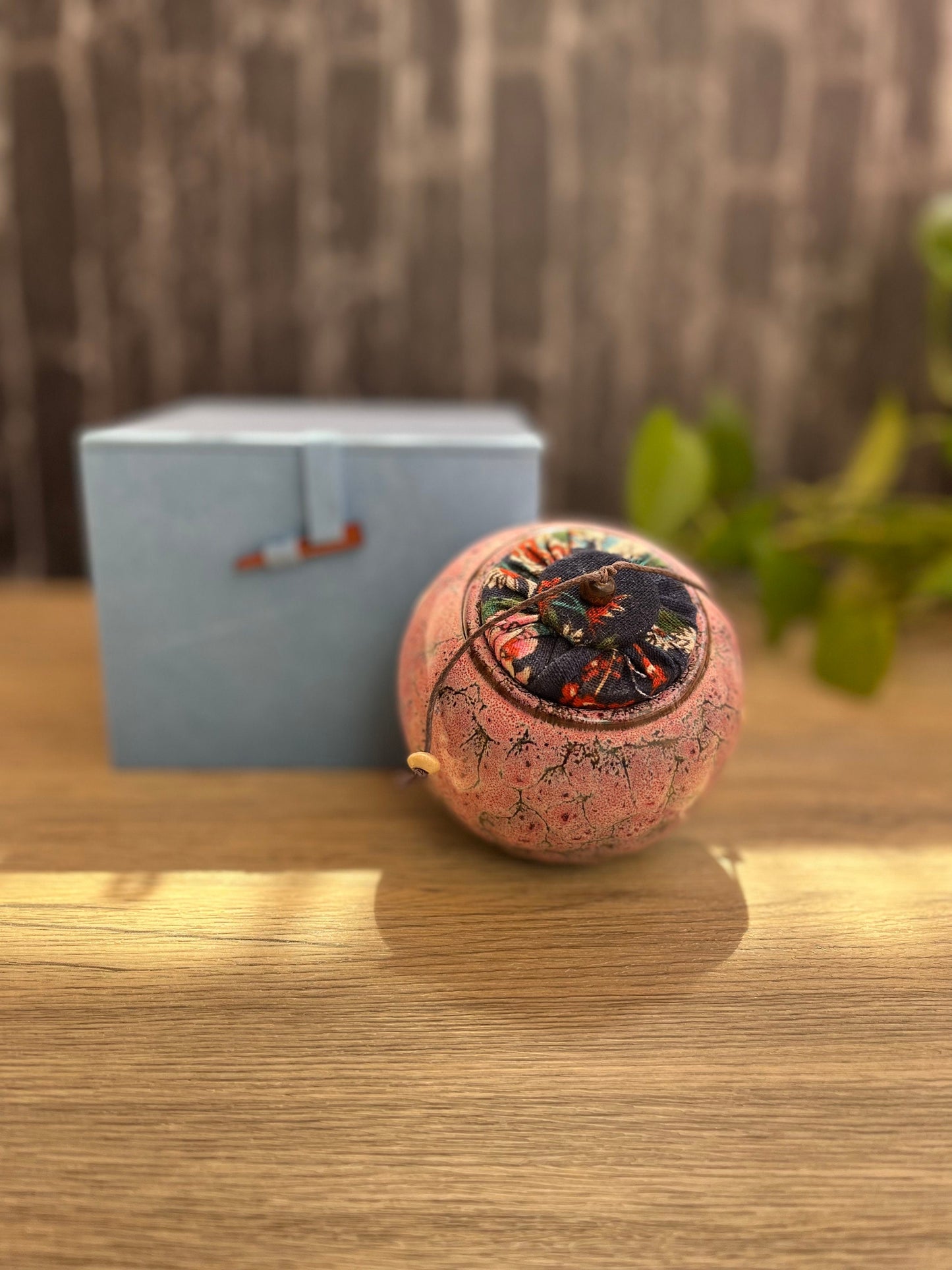 Round ceramic storage jar with natural glaze finish and airtight cloth wrapped lid in front of the blue gift box. The set is placed on a wooden table