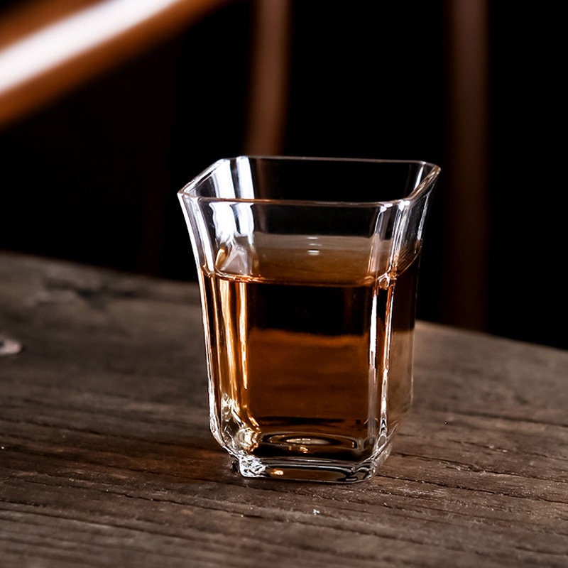 Small glass tea cup filled with amber-colored tea on rustic wood surface