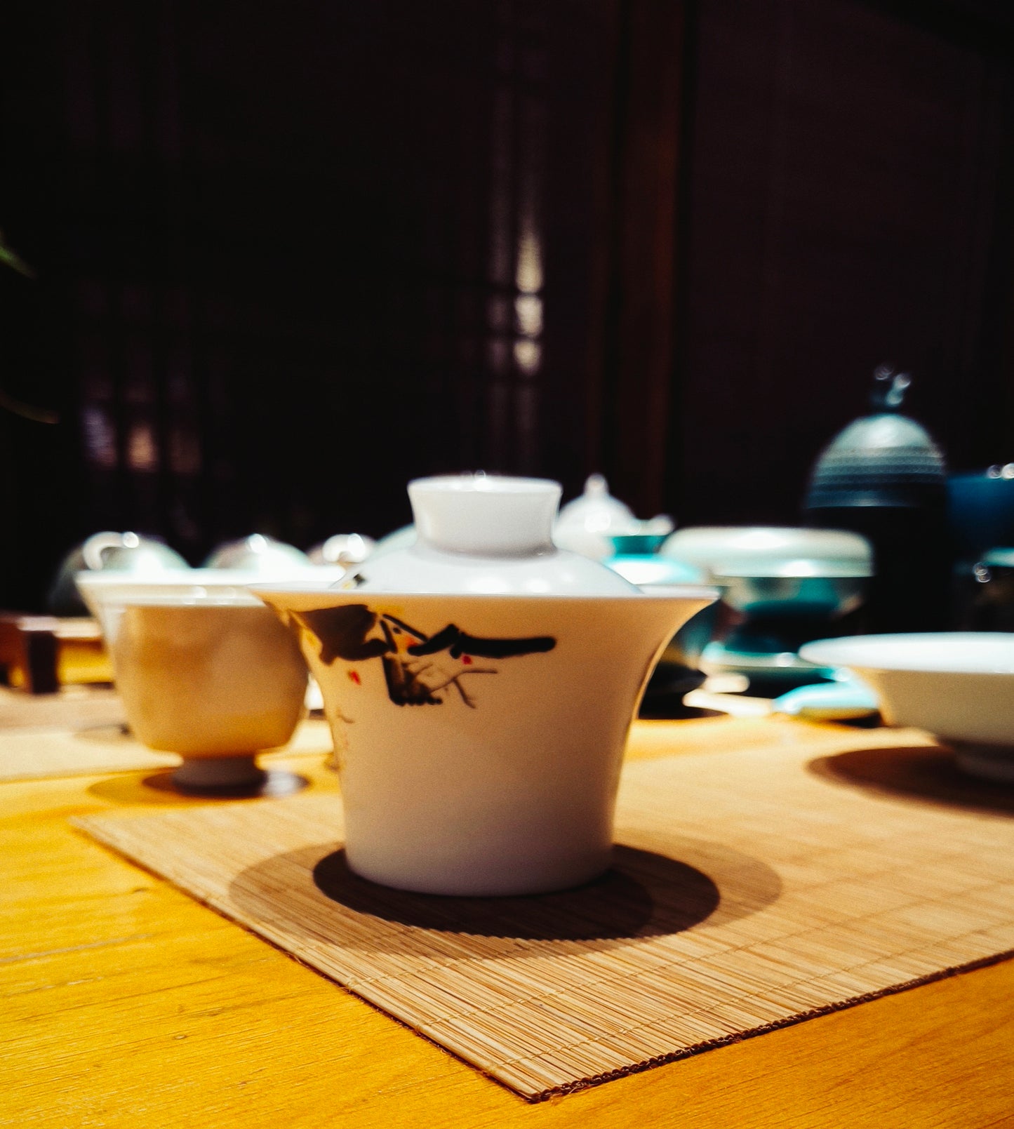 Hand-painted gaiwan with abstract Chinese brushwork, placed on a bamboo tea mat,along with other traditional artistic teaware