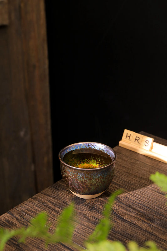 Rainbow glaze ceramic tea cup filled with tea on rustic ancient feel table_by Home Relax Studio