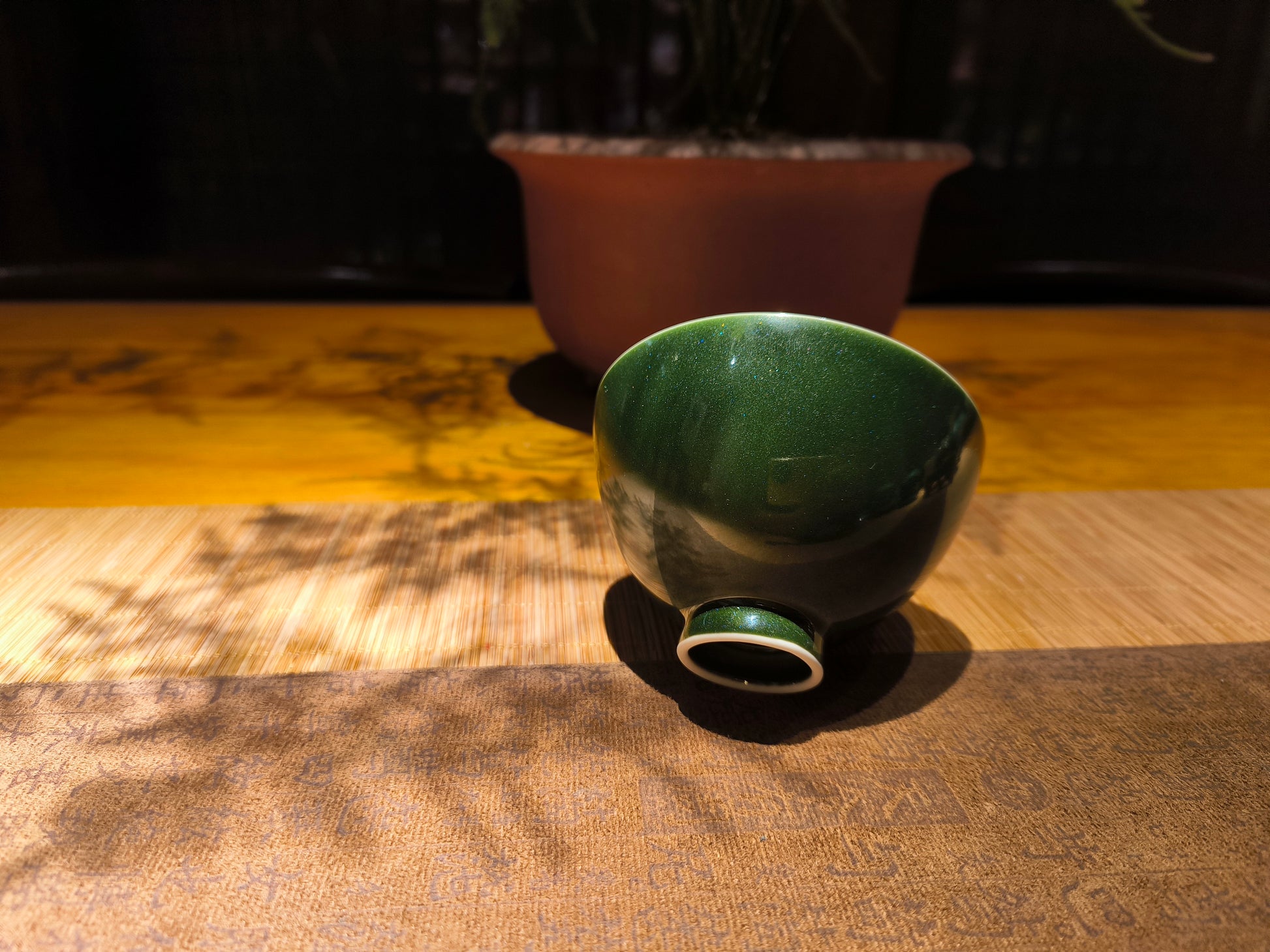 Side angle of handcrafted underglaze teaware cup showing sparkling glaze in light, traditional Asian table background, zen vibe with luxe feel