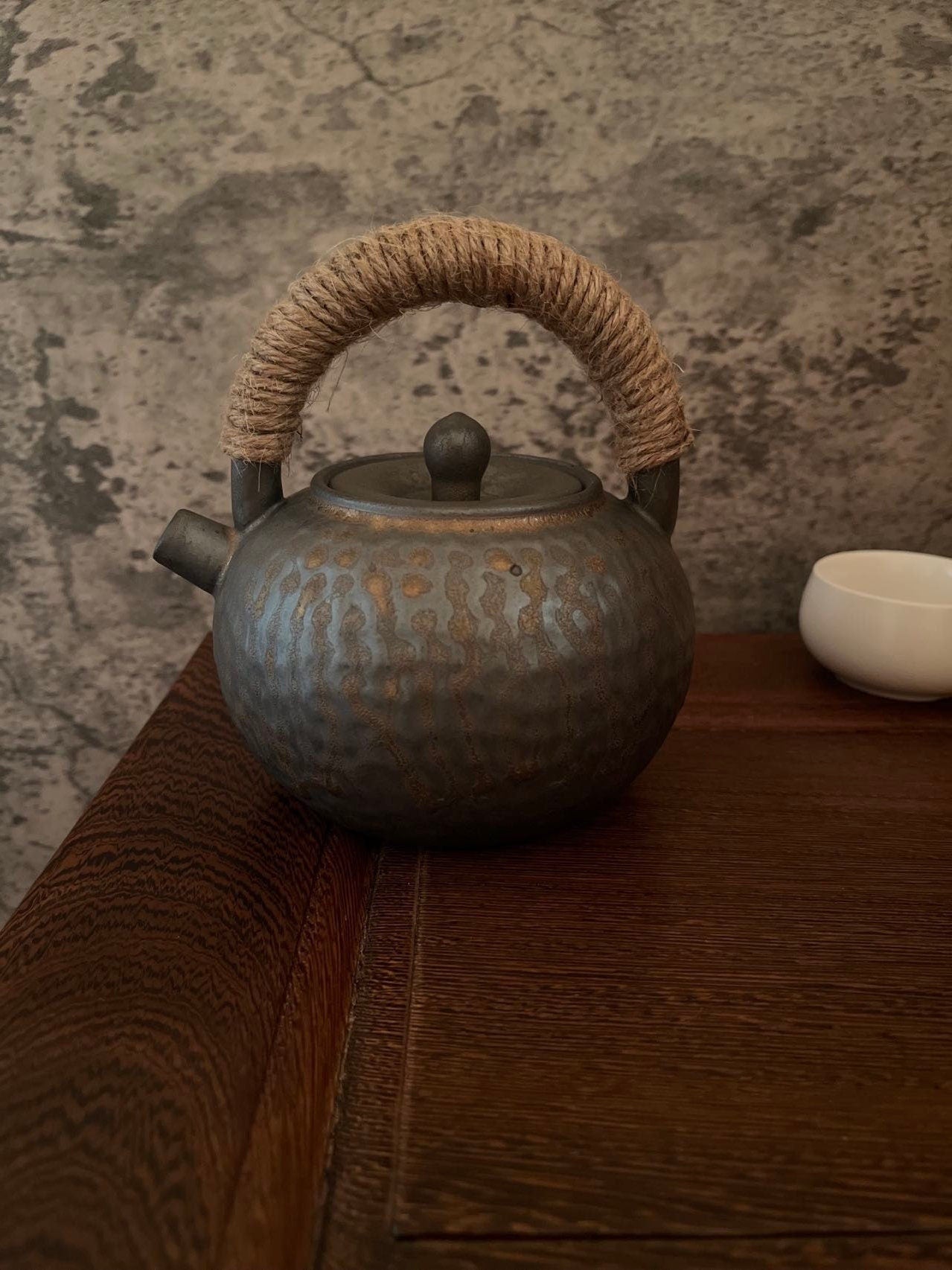 An old-fashioned gray ceramic teapot with a rustic handle design, placed on a wooden surface. Elegant Zen style ceramic teapot with rope handle on wooden table