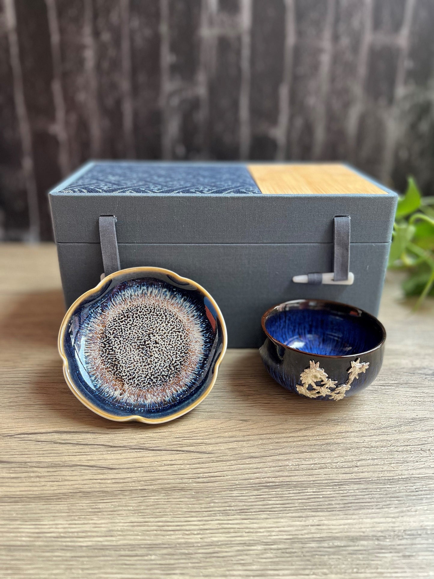 Blue ceramic tea cup with  floral embellishments design and matching dish displayed in front of a luxe gift box, made by Home Relax Studio.