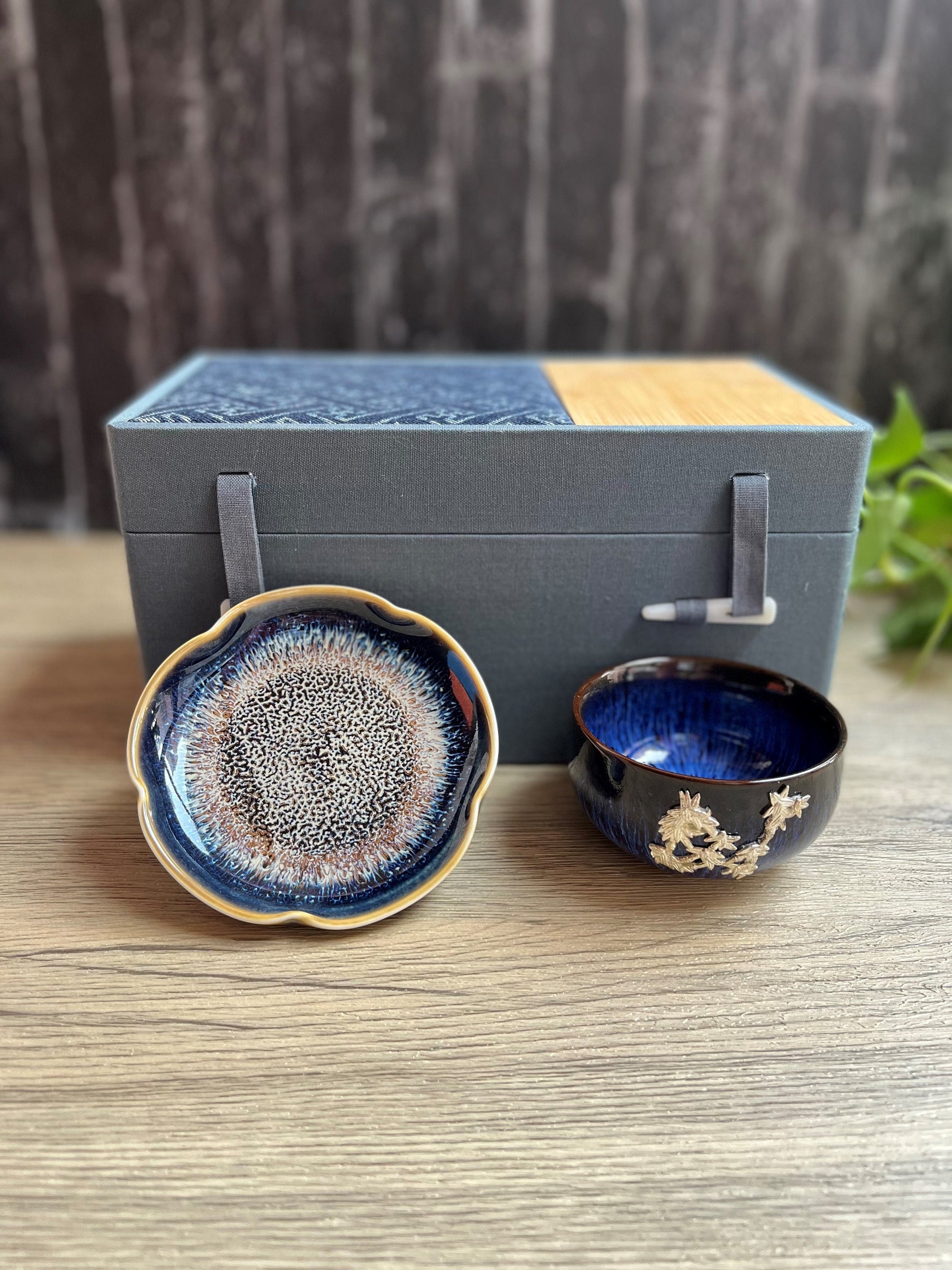Blue ceramic tea cup with  floral embellishments design and matching dish displayed in front of a luxe gift box, made by Home Relax Studio.