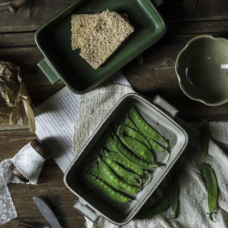 Ceramic baking tray with handles styled on dining table, trays filled with green beans and a piece of cake