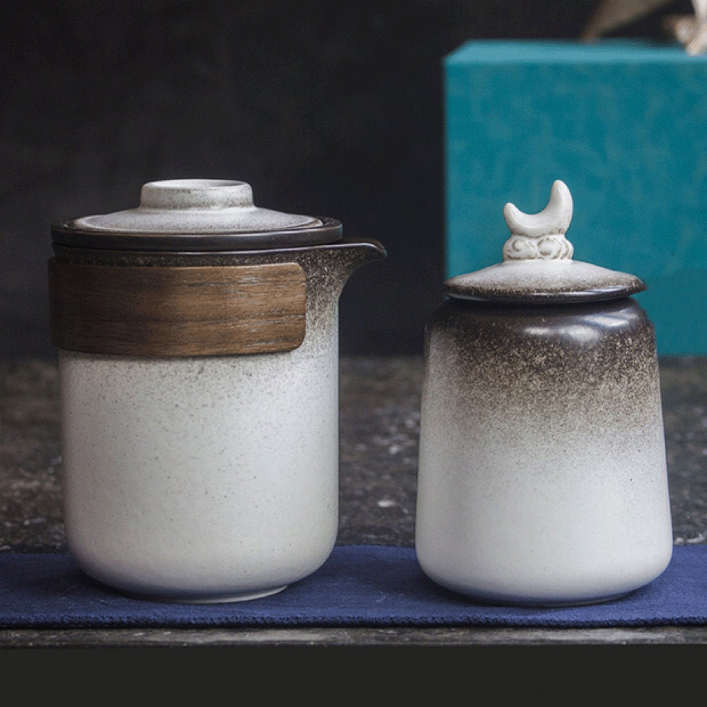 Ceramic tea kettle with wooden sleeve and matching tea cups on table