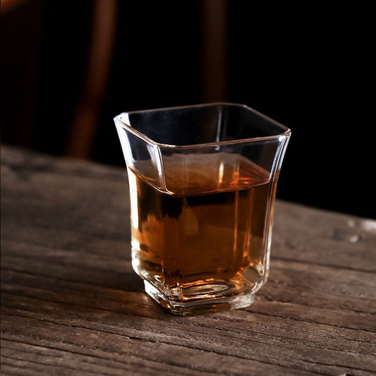 Clear borosilicate glass mini tea cup filled with tea on wooden surface by Home Relax Studio