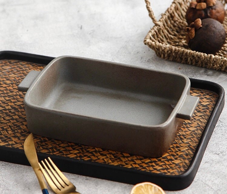 Empty ceramic baking dish with rustic handles on woven mat