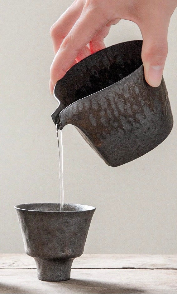Hand pouring milk from vintage ceramic jug into small tea cup