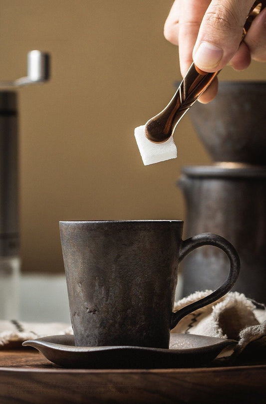 Hand pouring sugar into rustic ceramic espresso cup with saucer