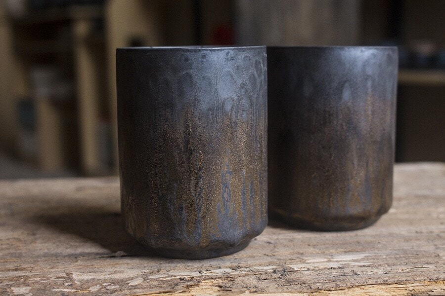 Two handcrafted can-shaped ceramic tea cup with silver-blue glaze and golden rustic pattern, side by side