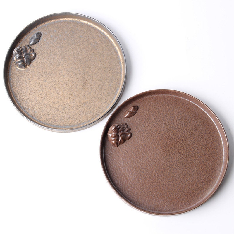 Overhead view of two ceramic tea plates in silver and brown tones.