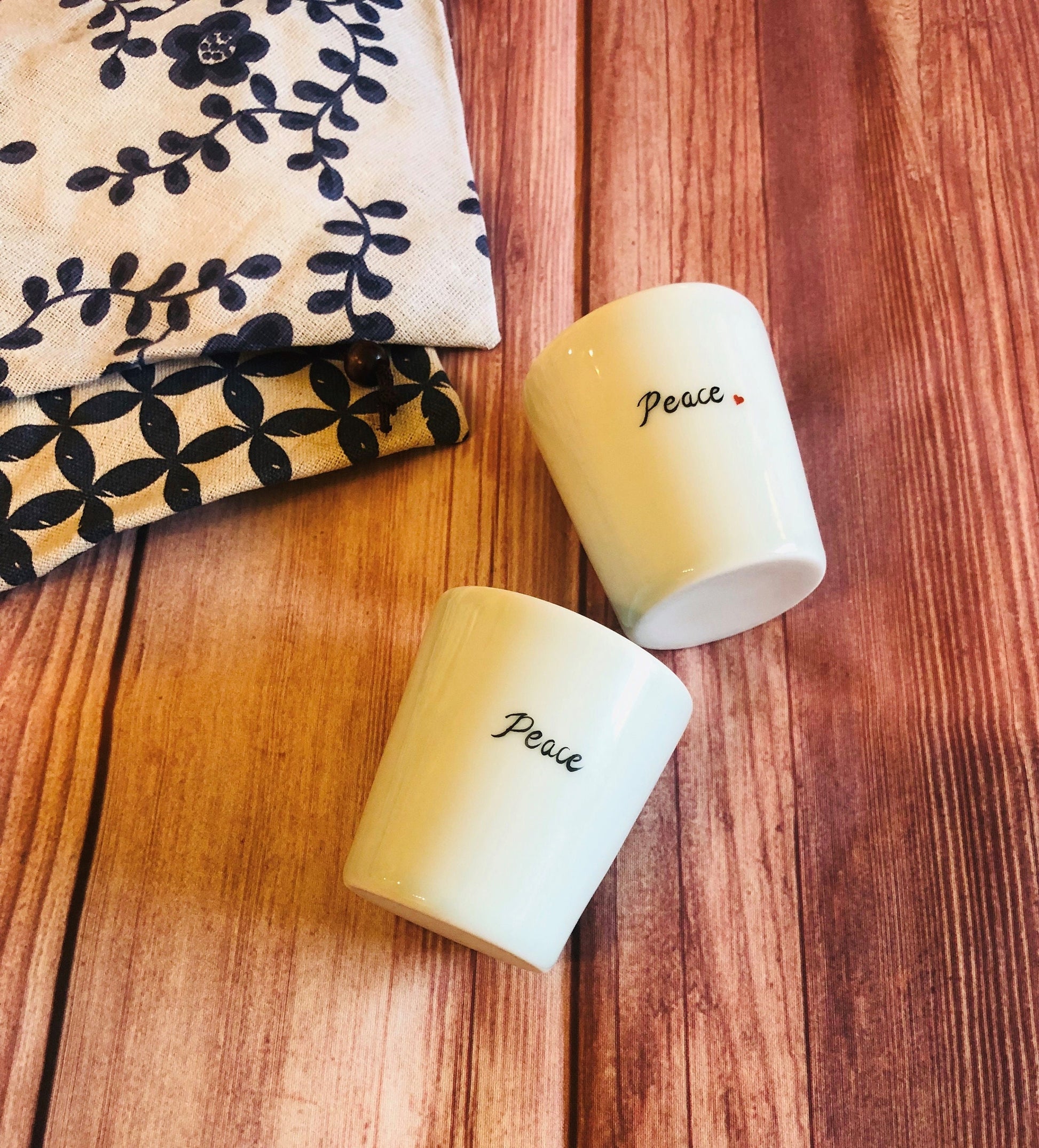 Pair of white ceramic mini cups with handwritten words on wooden surface; one of them has a red heart on it