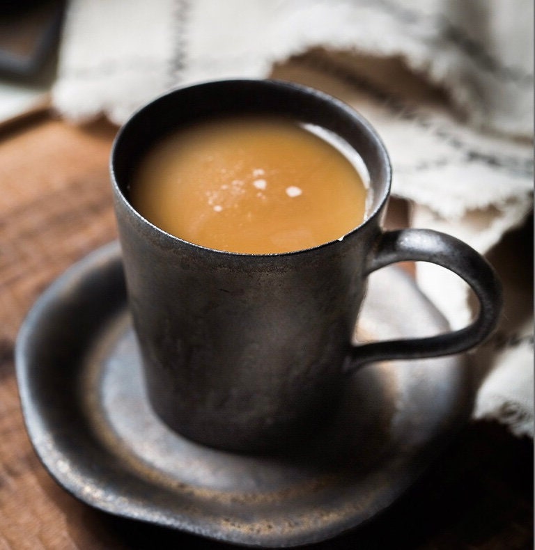 Small ceramic mug with retro glaze and saucer for espresso, placed on round irregular unique shaped retro style matching plate