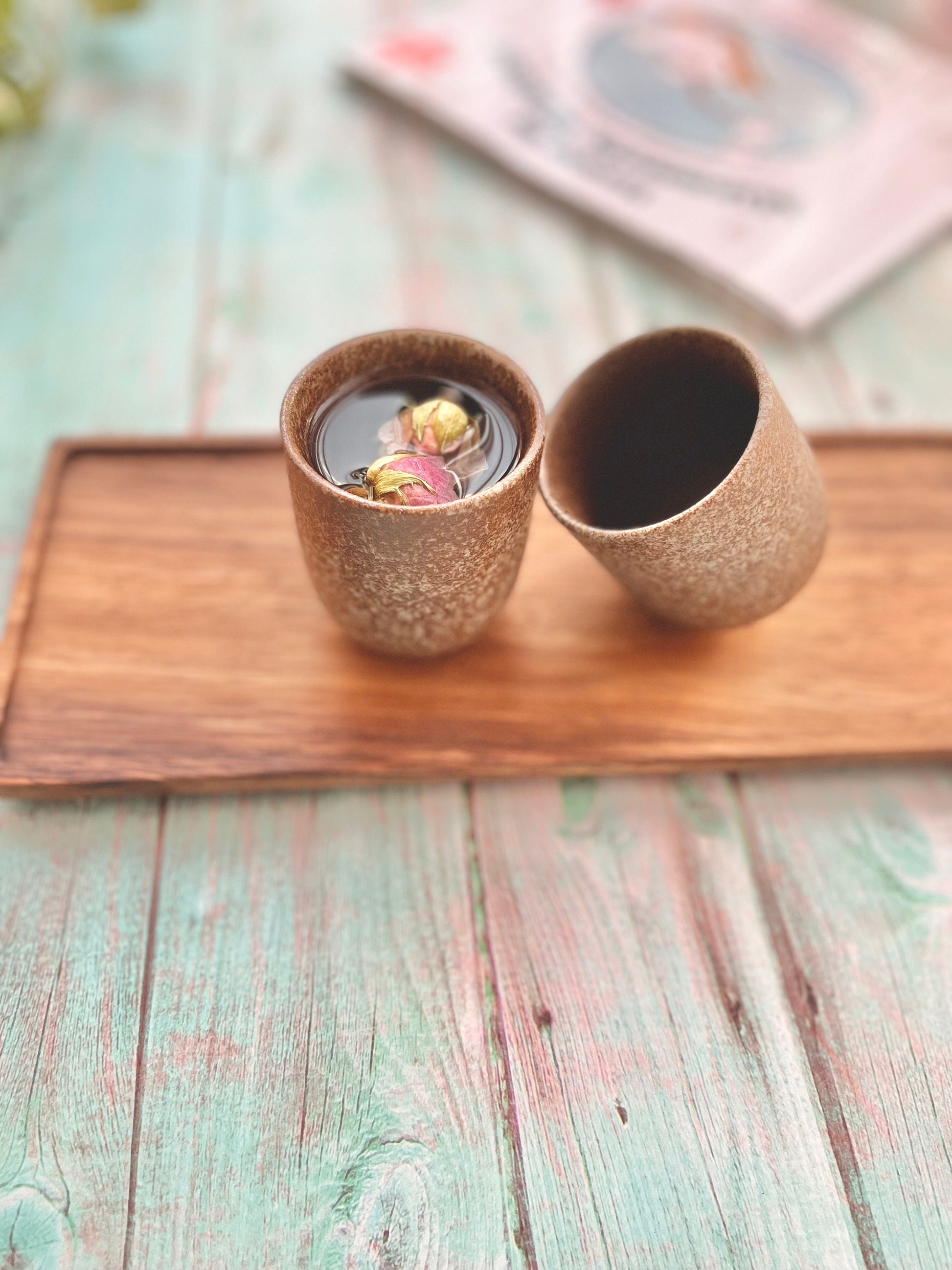 Two minimalist Japanese style ceramic tea cups with speckled glaze on wooden tray, filled with drinkable rose water_styled on pastel blue rustic table – Home Relax Studio